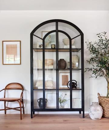 Modern transitional shelving unit in black with arched top, styled with curated objects and greenery