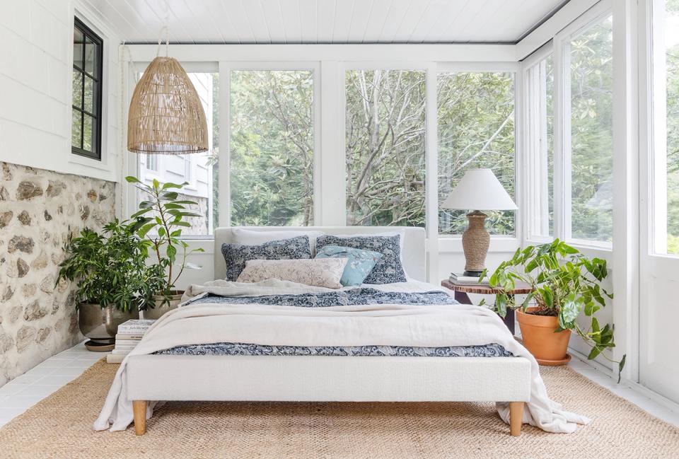 Serene bedroom with white walls, patterned blue bedding, abundant plants, and warm wood accents for peaceful escape.