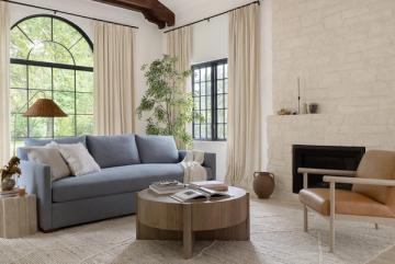 Serene contemporary space with soft blue sofa, neutral tones, arched windows, and organic botanical accents