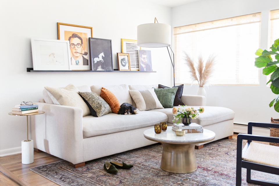 Minimalist living room with cream sectional, round brass coffee table, and warm neutral palette with gallery wall
