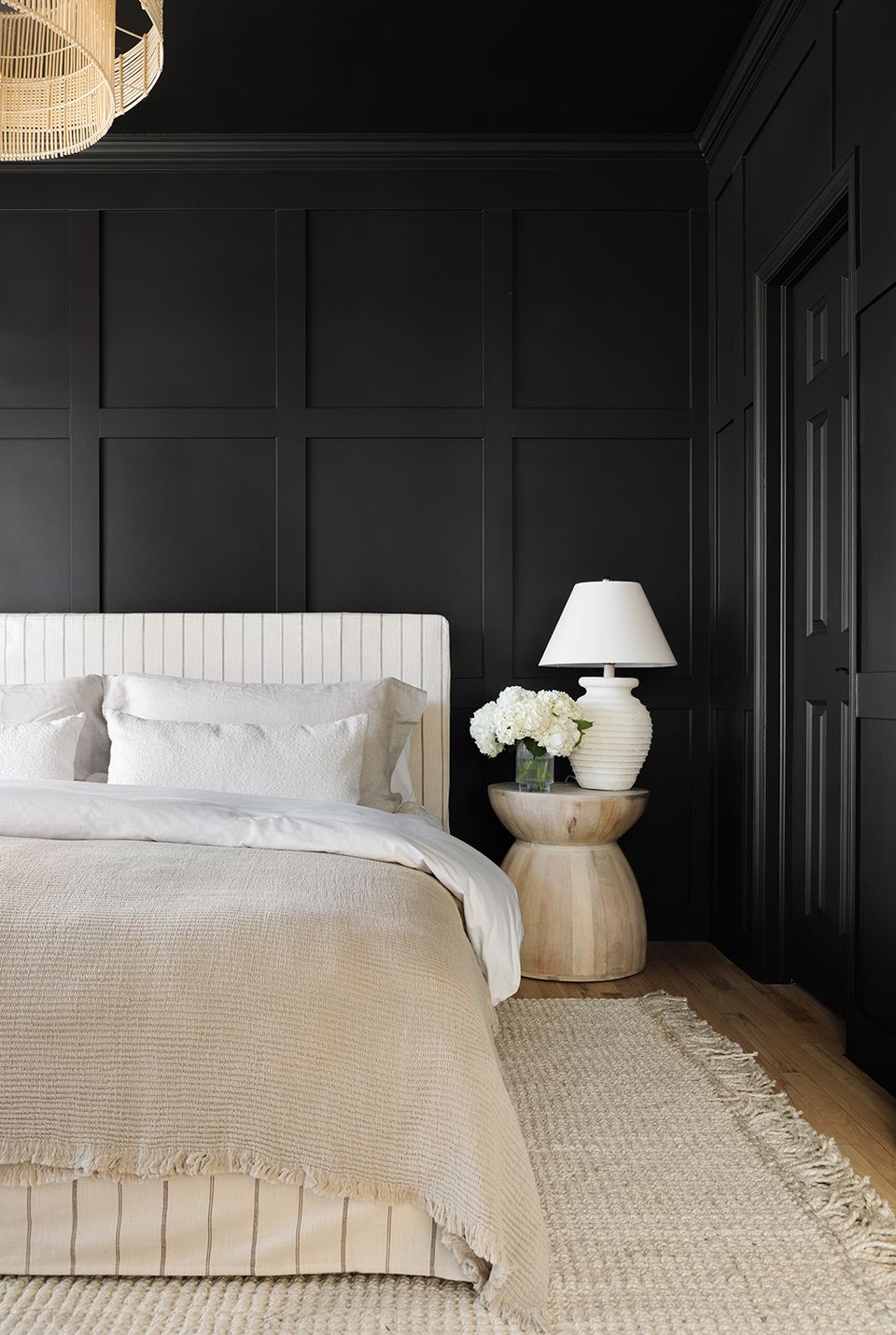 Modern boho bedroom with black paneled walls, cream bed, and natural wood side table