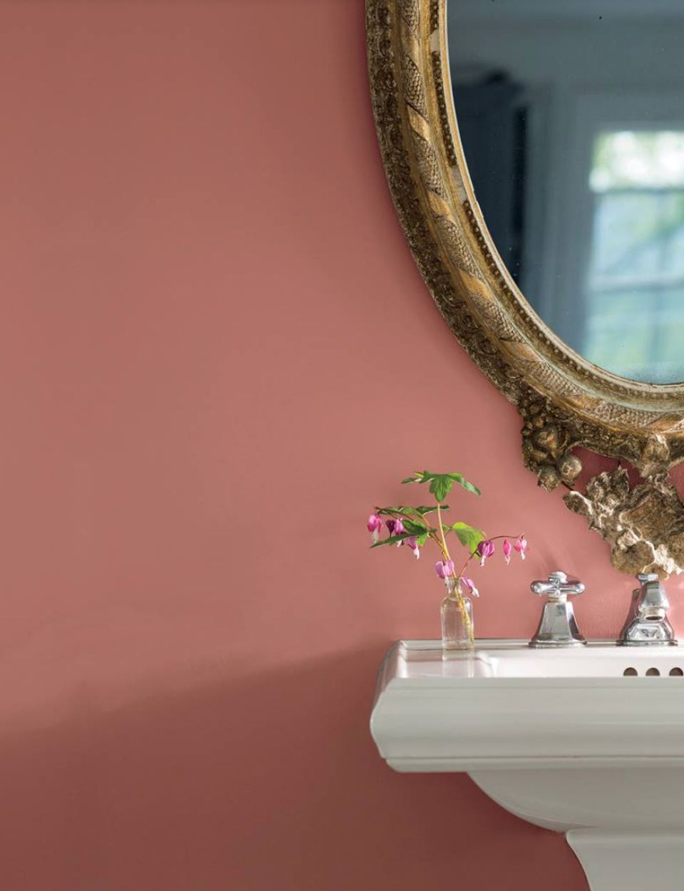 Romantic blush pink bathroom wall with ornate gold-framed mirror and white marble shelf with fresh flowers