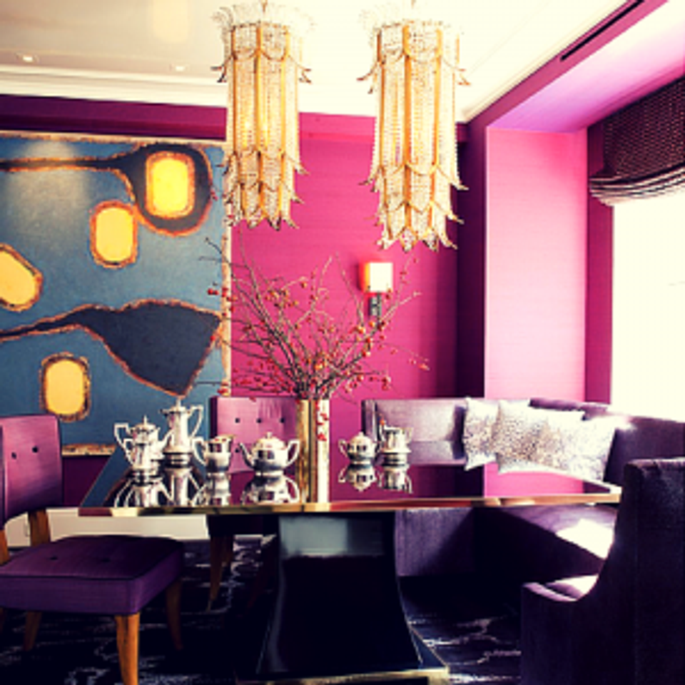 Bold maximalist lounge: magenta walls, navy seating, brass chandeliers, and saturated jewel tones