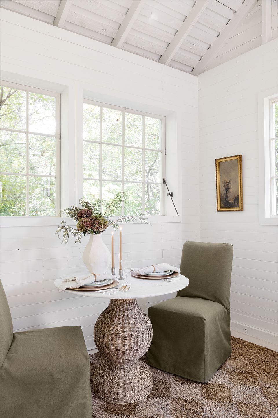 Light-filled breakfast nook with white paneling, sage chair slipcover, woven side table, and abundant natural light