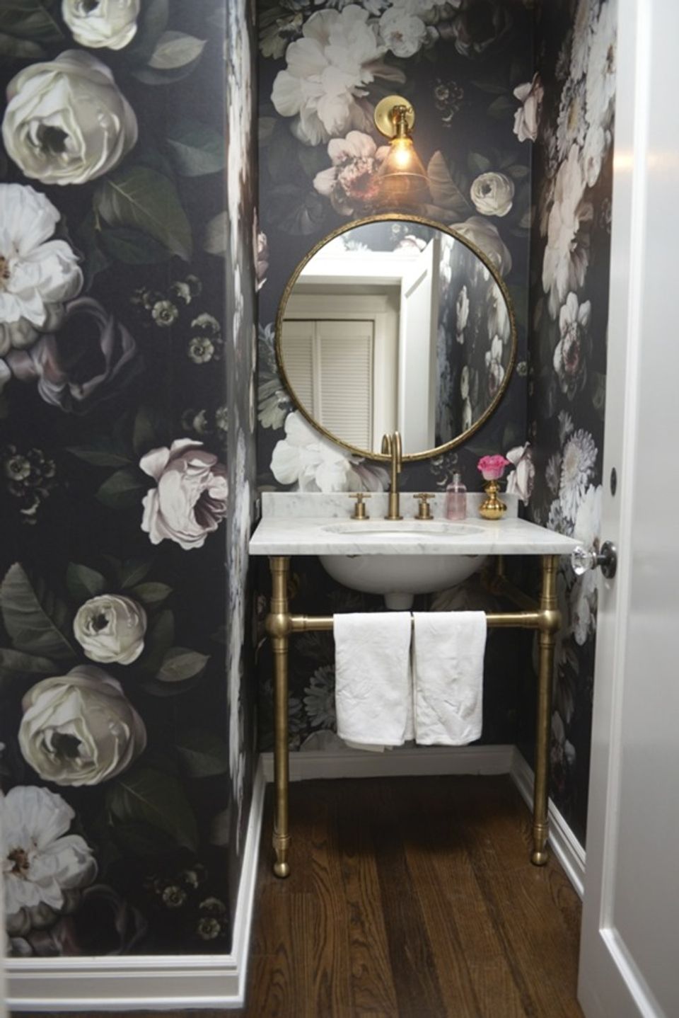 Dramatic dark floral powder room with round gold mirror and moody botanical wallpaper
