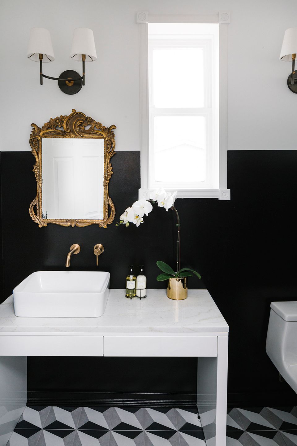 Eclectic bathroom mixing black-and-white geometric tile, gold ornate mirror, brass fixtures, and contemporary wall sconces