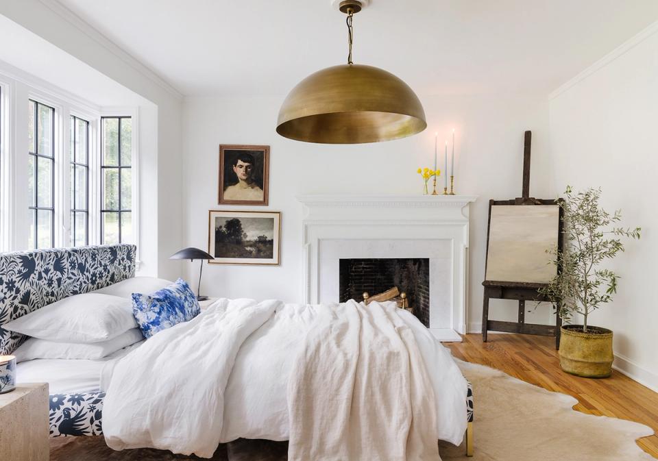 Serene bedroom with brass pendant, fireplace, blue accents, and airy white bedding.