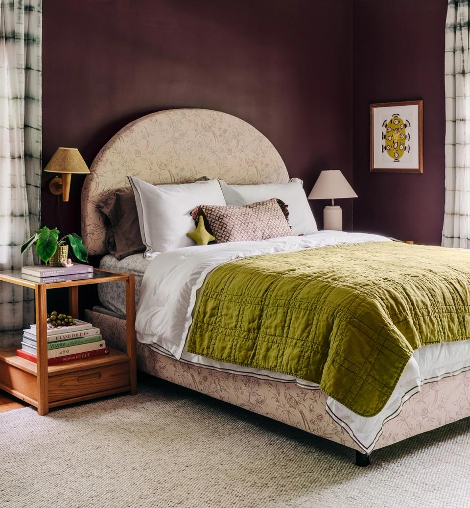 Jewel-tone bedroom with deep burgundy walls, chartreuse bedding, curved headboard, and warm wood nightstand