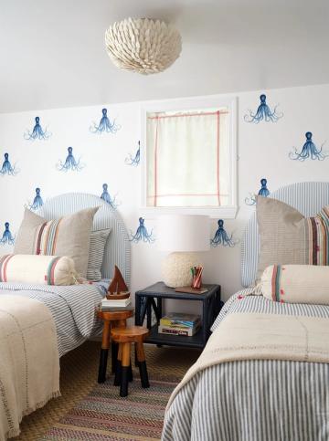 Coastal bedroom with blue nautical wallpaper, striped bedding, and serene white backdrop
