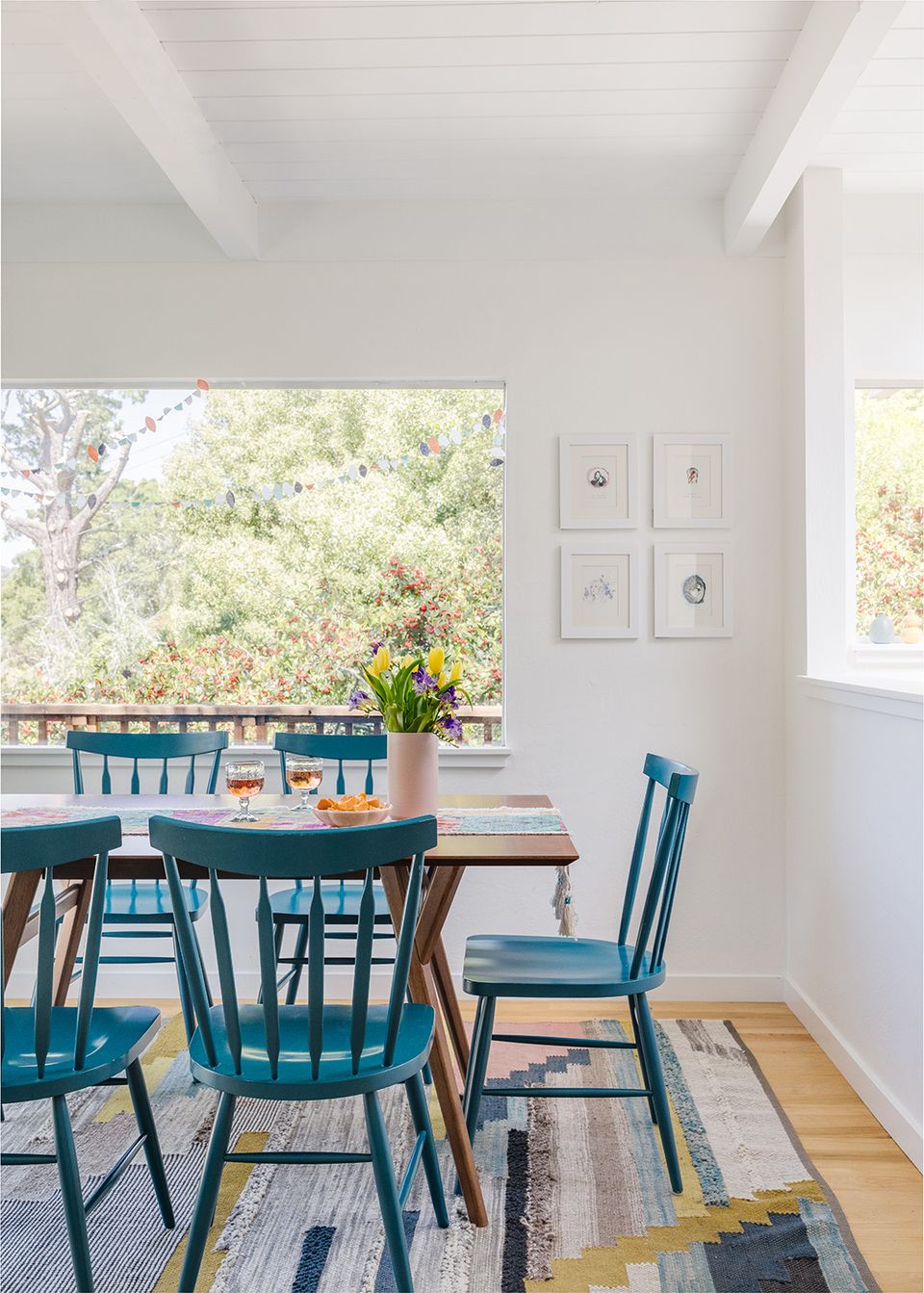 Coastal dining space with teal chairs, natural wood table, and geometric area rug