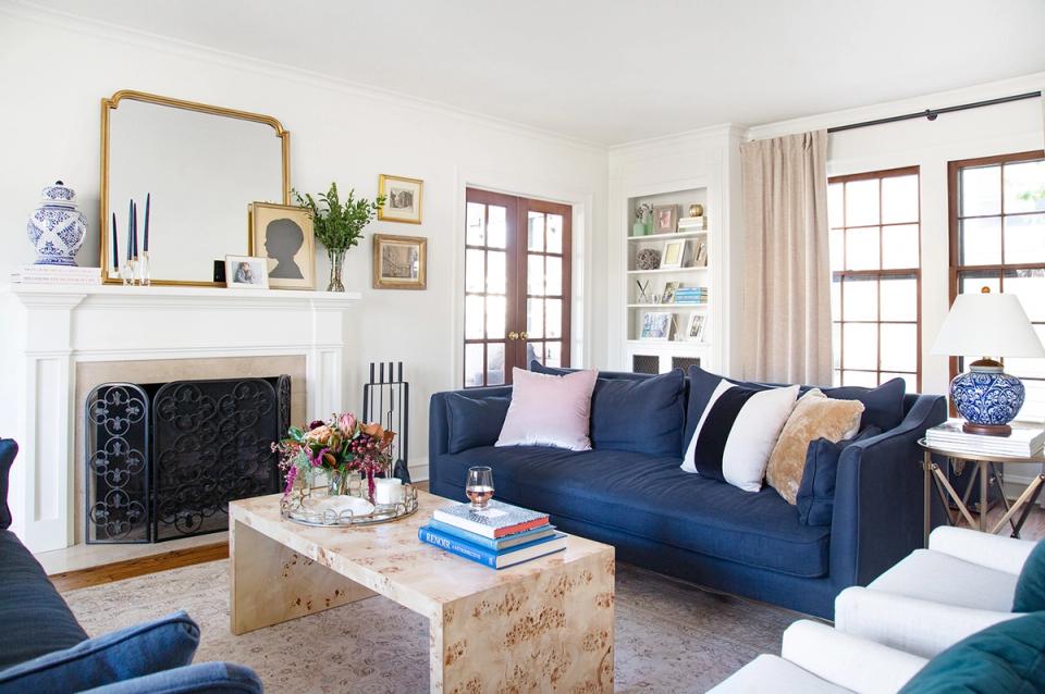 Classic transitional living room featuring rich navy velvet sofa, white fireplace mantel, and blue ceramic accents