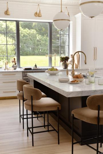 Modern elegant kitchen with white cabinetry, dark island, natural leather seating, and abundant natural light