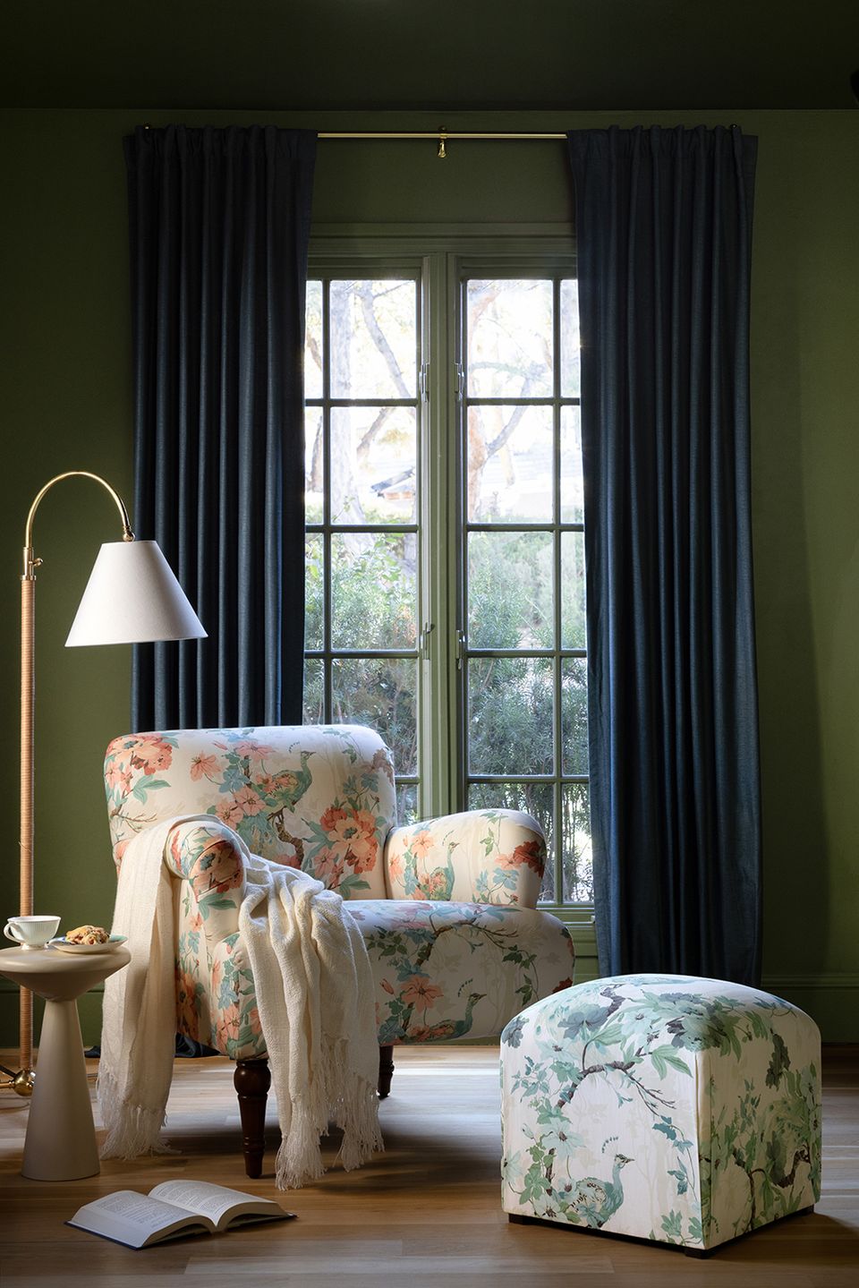 Sophisticated reading corner with deep forest green walls, navy floor-to-ceiling curtains, floral-print wingback chair, and brass arc lamp creating moody traditional charm.