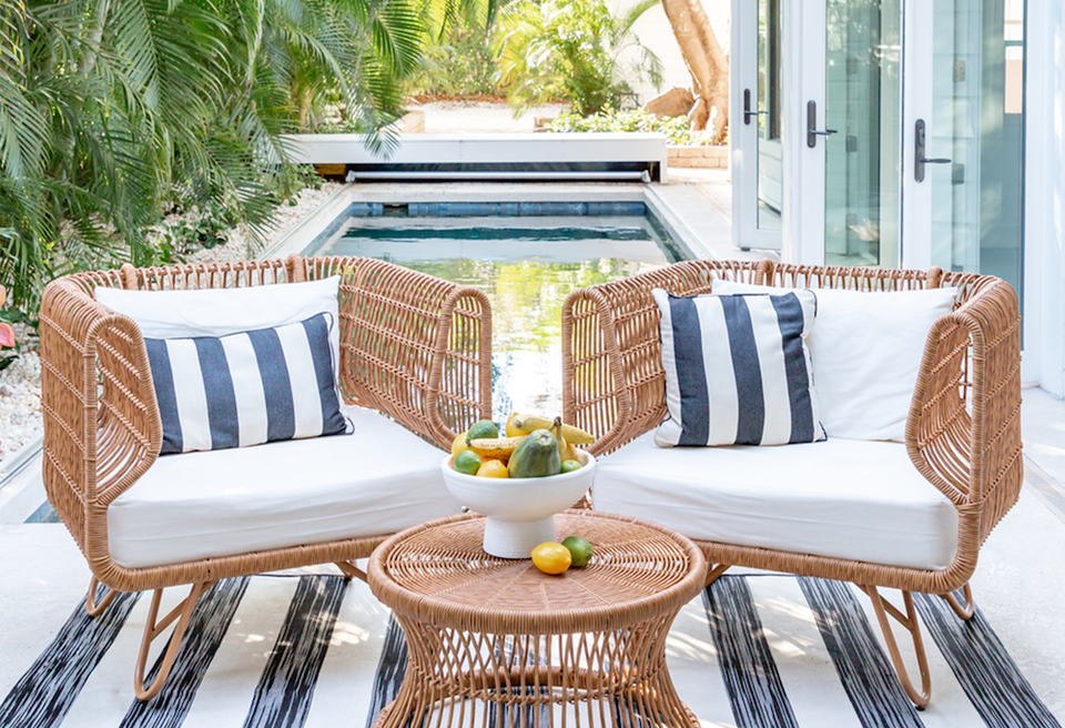 Tropical coastal patio with woven rattan seating, navy striped pillows, and serene poolside ambiance