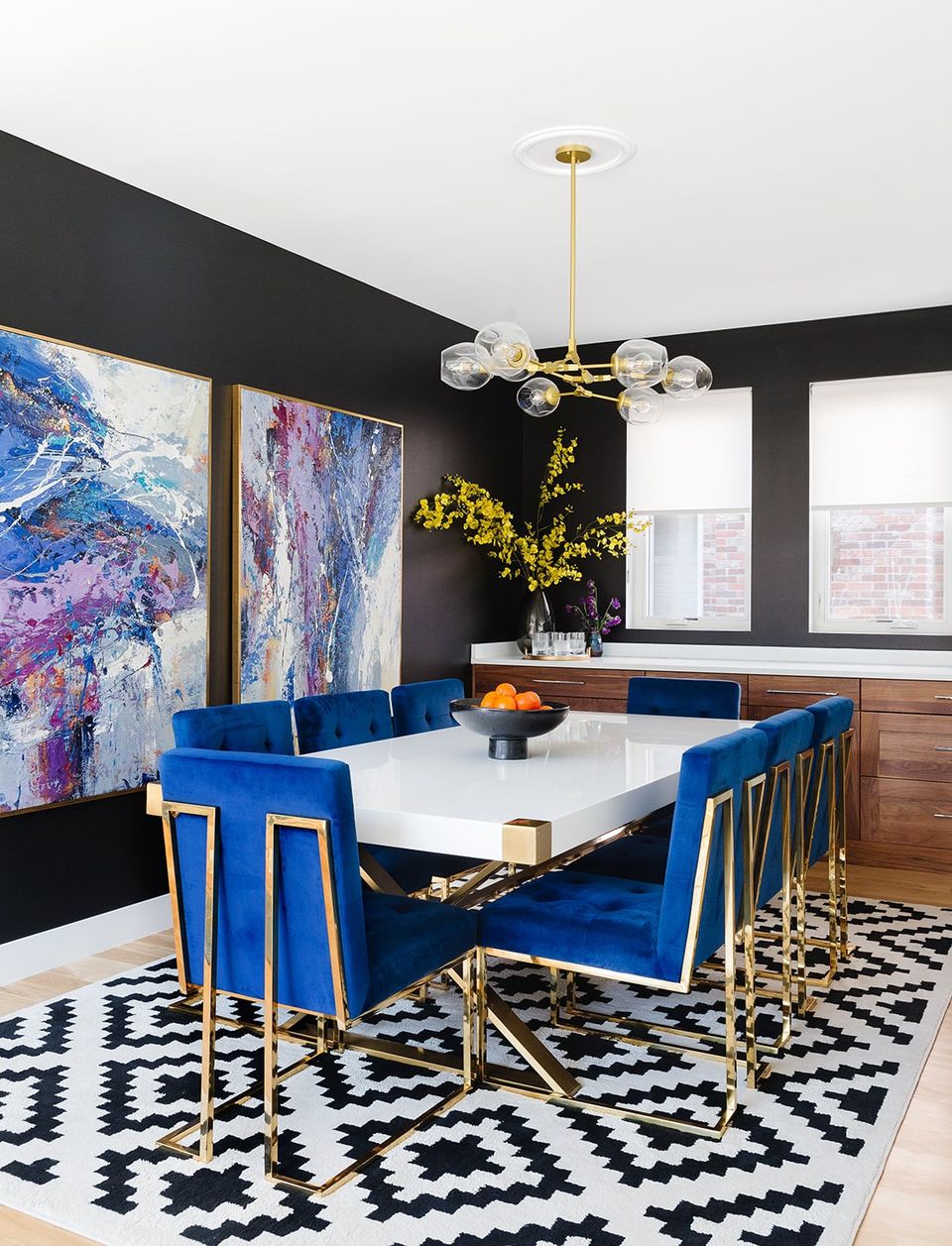 Bold contemporary dining with cobalt blue chairs, black walls, white table, geometric pattern rug, and art accents