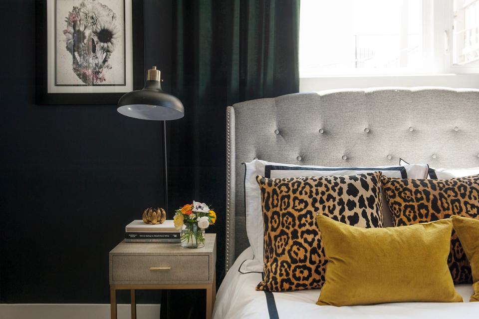 Moody bedroom with deep green walls, leopard print throw, and mustard yellow accent pillow.