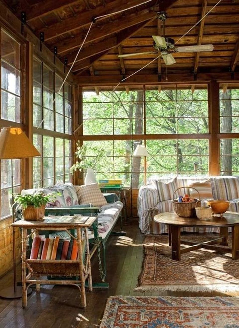 Sunlit screened porch with wood beams, striped upholstery, vintage rugs, and abundant natural light
