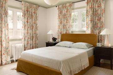 Bedroom with red floral curtains, golden headboard, cream bedding, and dark wood nightstands in traditional, warm design.