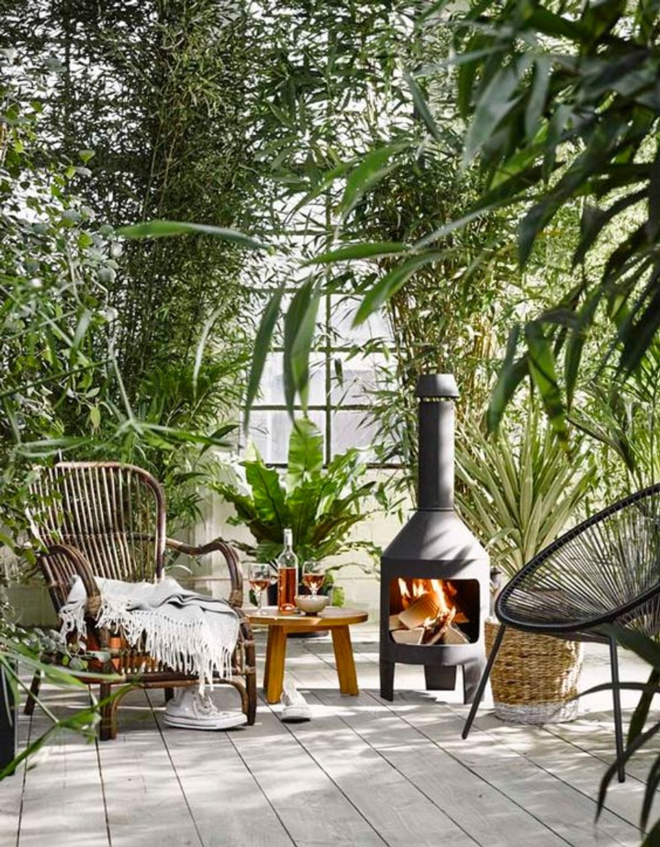 Bohemian patio with woven chairs, lush greenery, warm fireplace glow