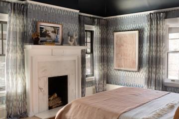 Modern traditional bedroom with black ceiling, geometric wallpaper, fireplace, and soft pink and wood tone accents