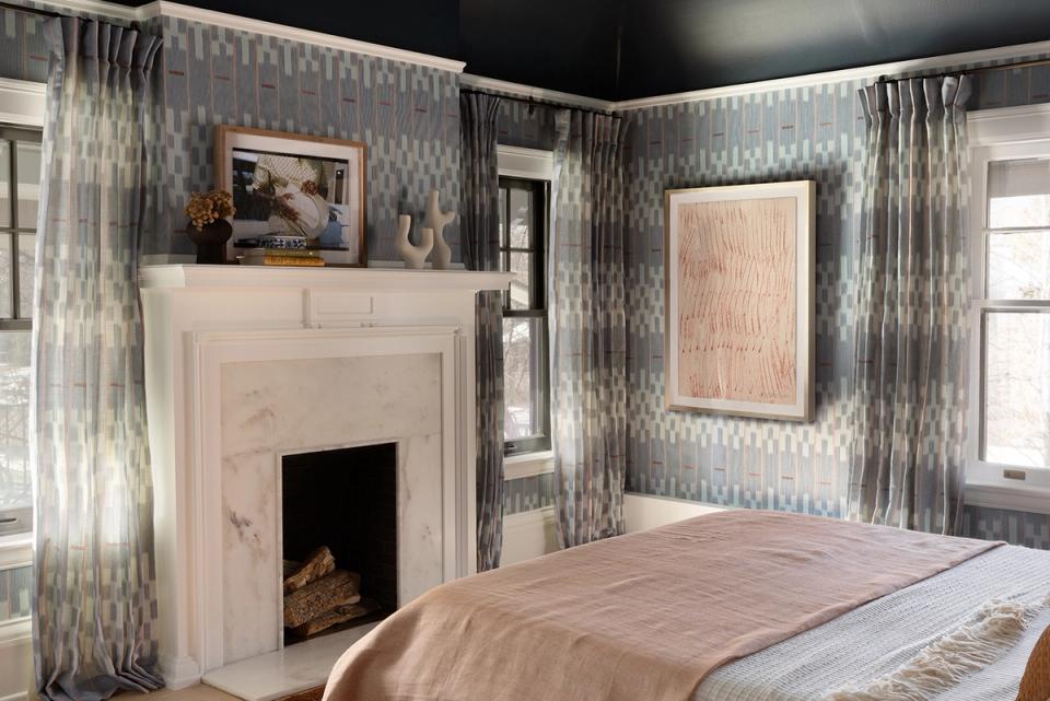 Modern traditional bedroom with black ceiling, geometric wallpaper, fireplace, and soft pink and wood tone accents