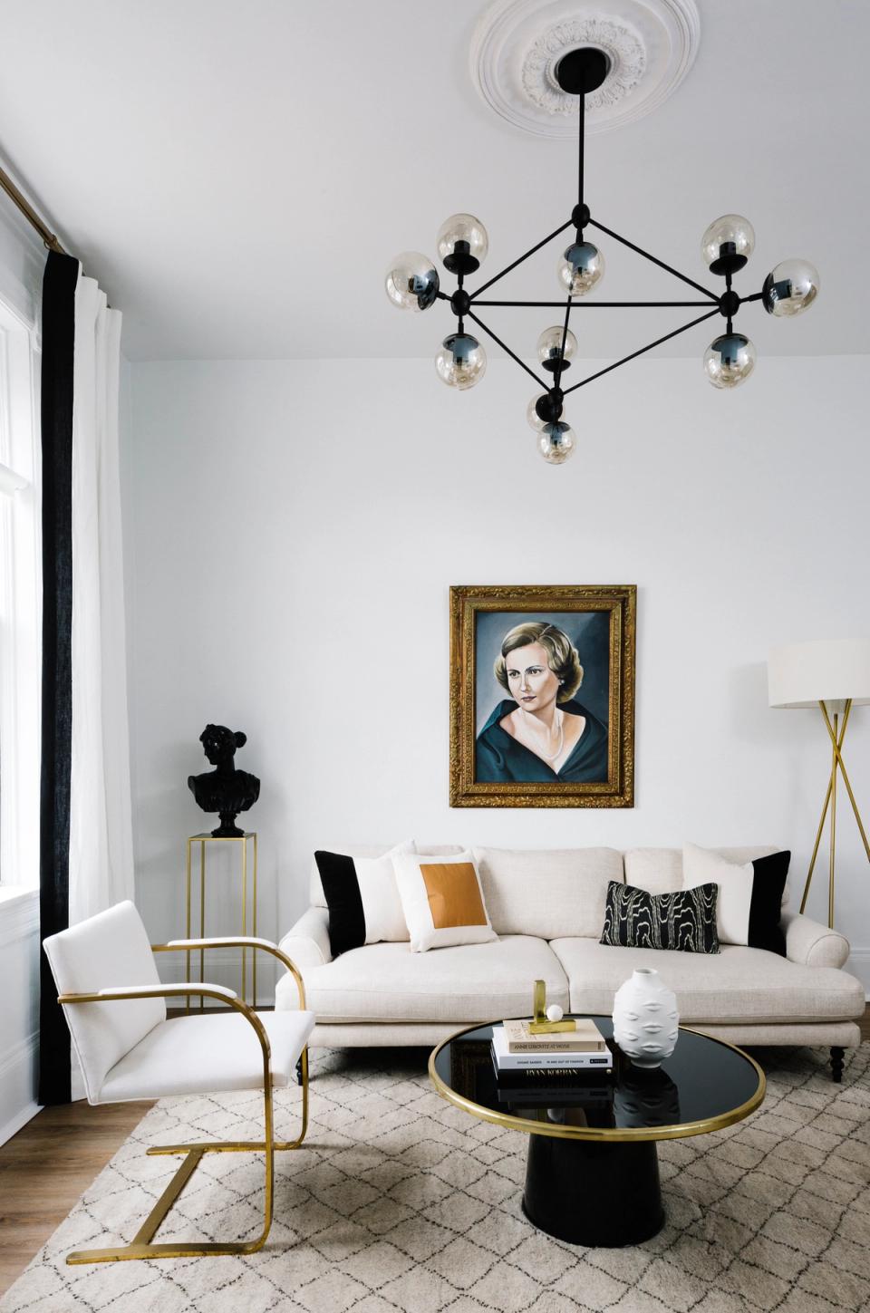 Modern living room with black and brass geometric chandelier, cream sofa, and curated gallery wall blending contemporary and vintage elements