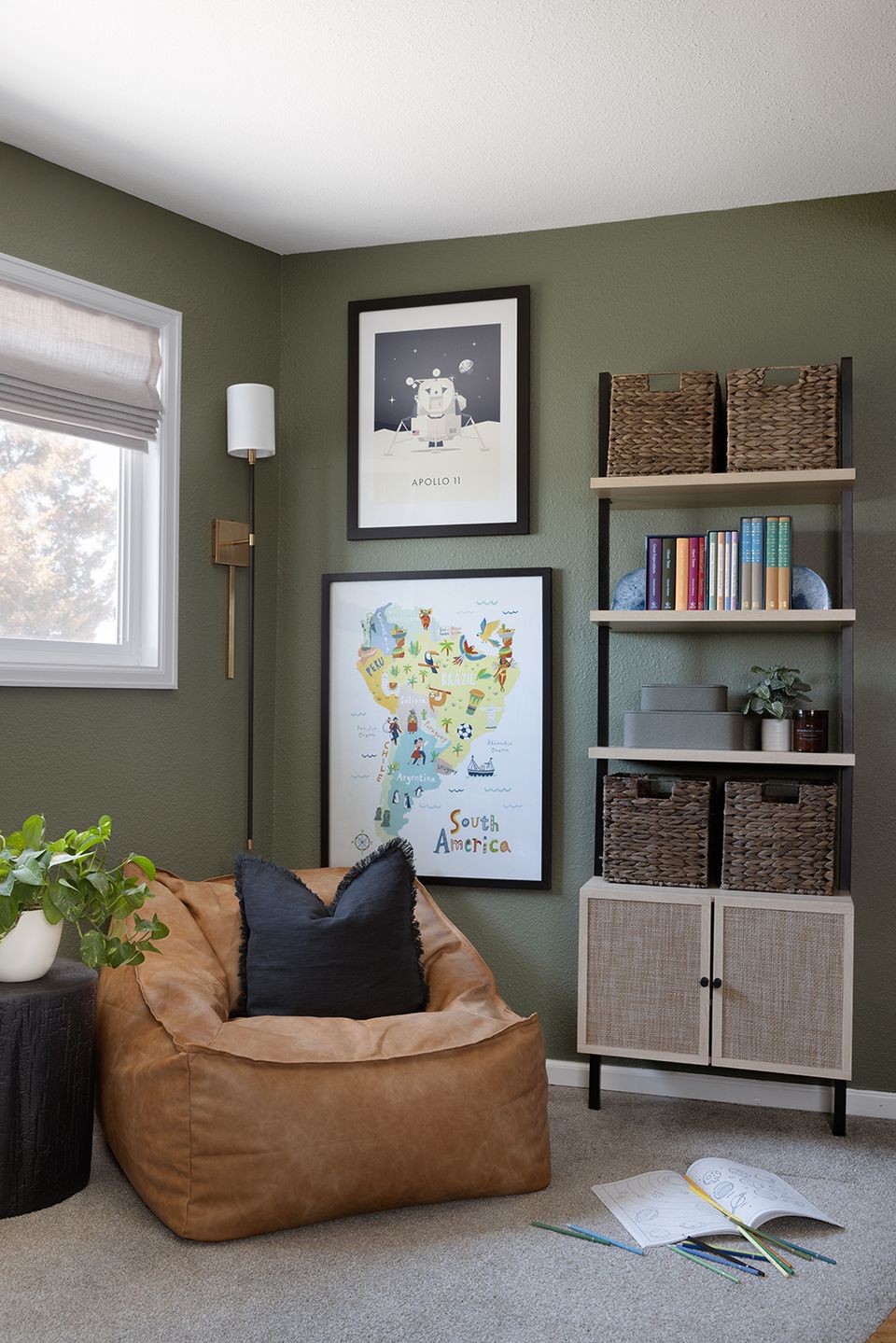 Tranquil olive-green reading corner with cognac chair, curated shelving, and botanical touches