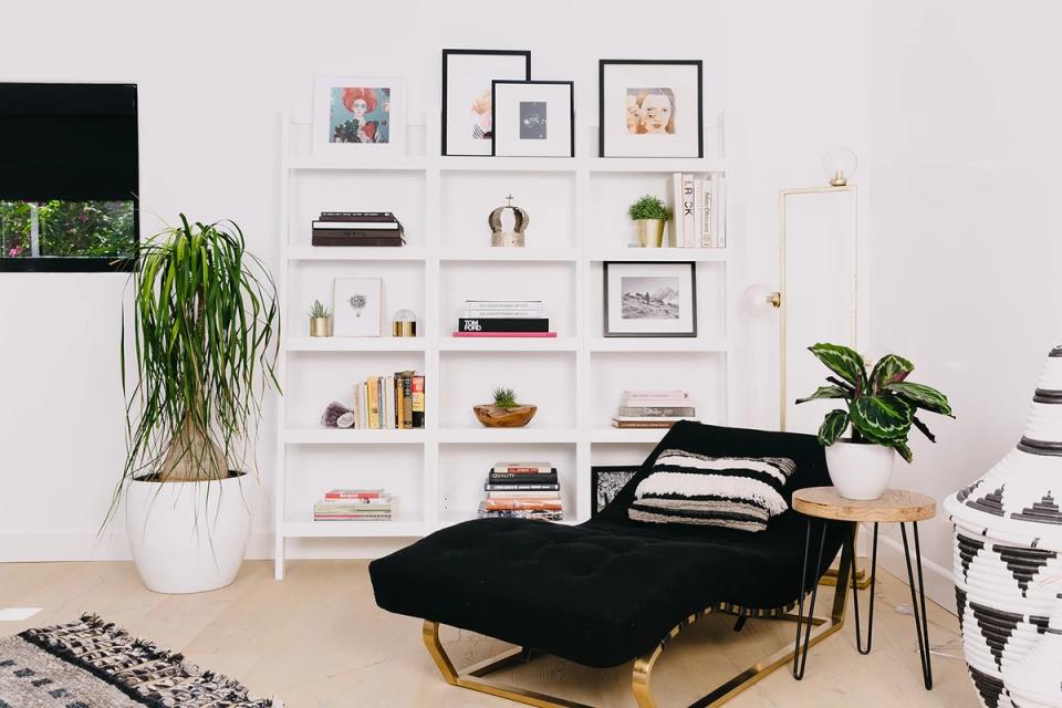 Minimalist bedroom with white floating shelves, black bed, potted plants, and curated book collection creating a calm, organized reading retreat.