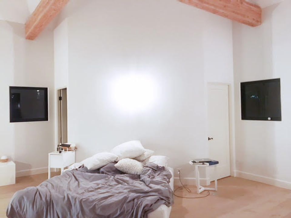 Industrial minimalist bedroom with exposed beam, warm grey bedding, and clean architectural lines