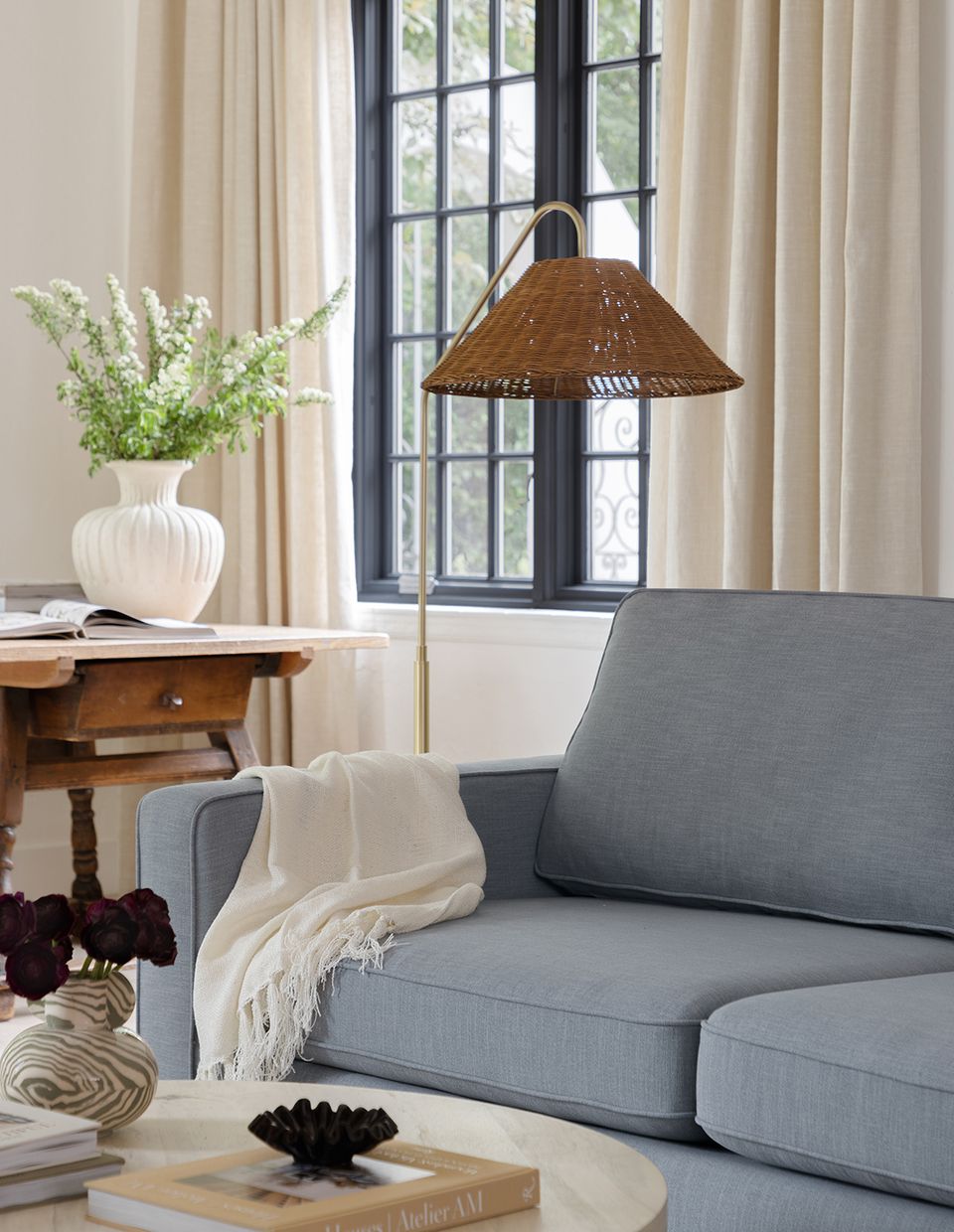Coastal-modern room with slate sofa, woven pendant, and cream drapery framing black-framed doors