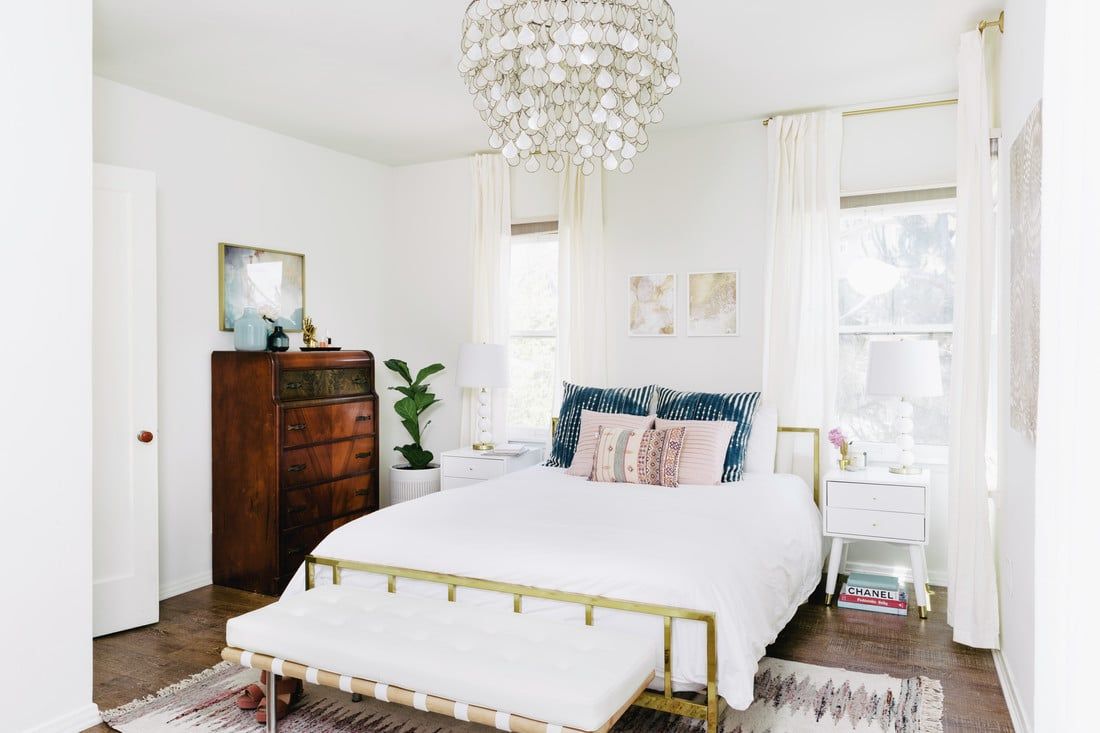 Bright bedroom with crystal chandelier, brass bed frame, and mix of mid-century and modern furnishings