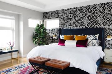 Modern bedroom with geometric black and white stenciled accent wall, navy bed frame, colorful throw pillows, and boho-inspired rug.