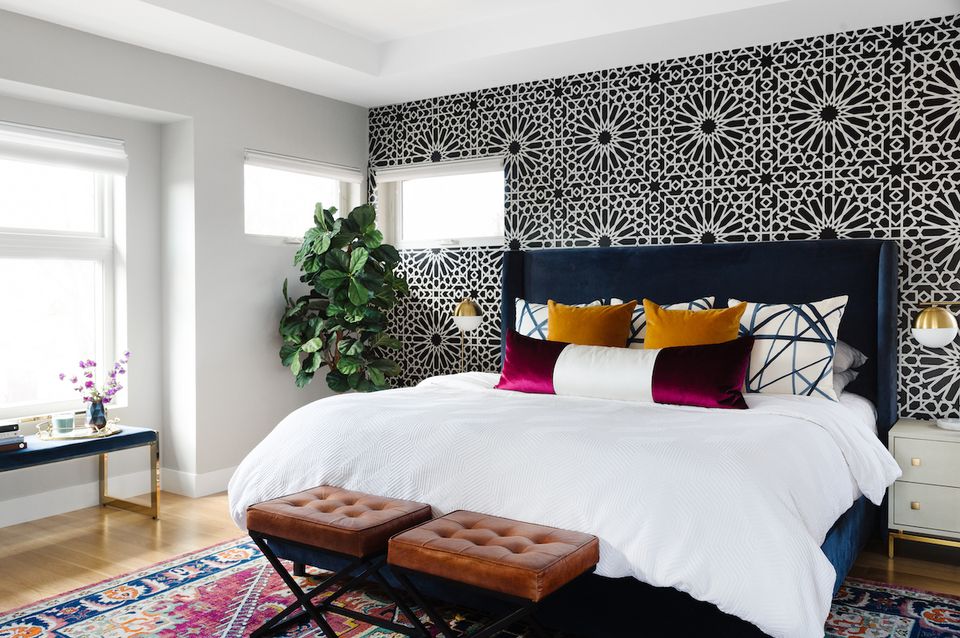Modern bedroom with geometric black and white stenciled accent wall, navy bed frame, colorful throw pillows, and boho-inspired rug.