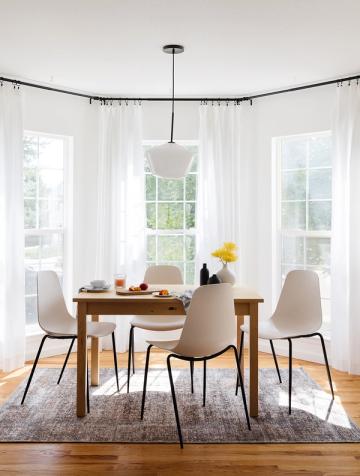 Minimalist dining area with flowing white curtains, curved pendant light, and natural wood table creating a clean, airy Scandinavian aesthetic.
