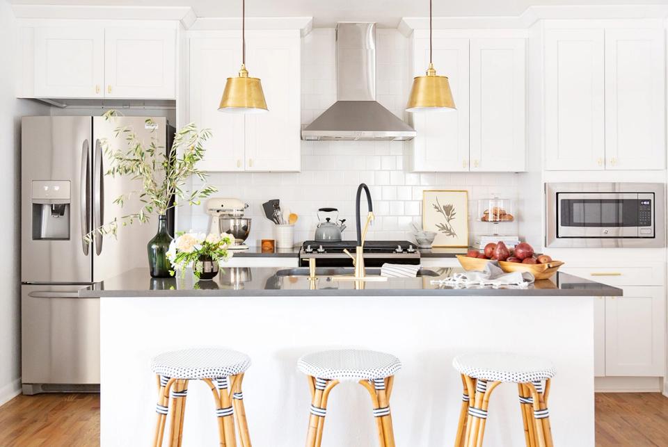 Bright contemporary kitchen with white cabinetry, gray island, woven bar stools, and brass accents