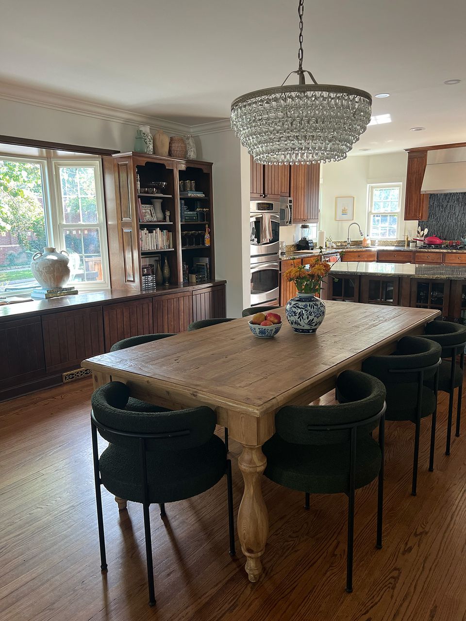 Open-concept kitchen with dark wood cabinetry, natural wood table, black chairs, and crystal chandelier