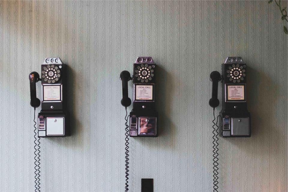Retro rotary phones mounted on textured wall with coiled cords, vintage aesthetic with muted earth tones