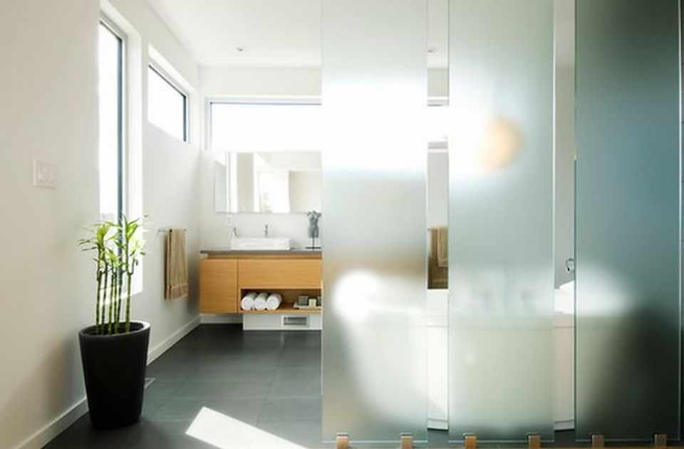 Minimalist bathroom with frosted glass shower, warm wood vanity, and clean white palette