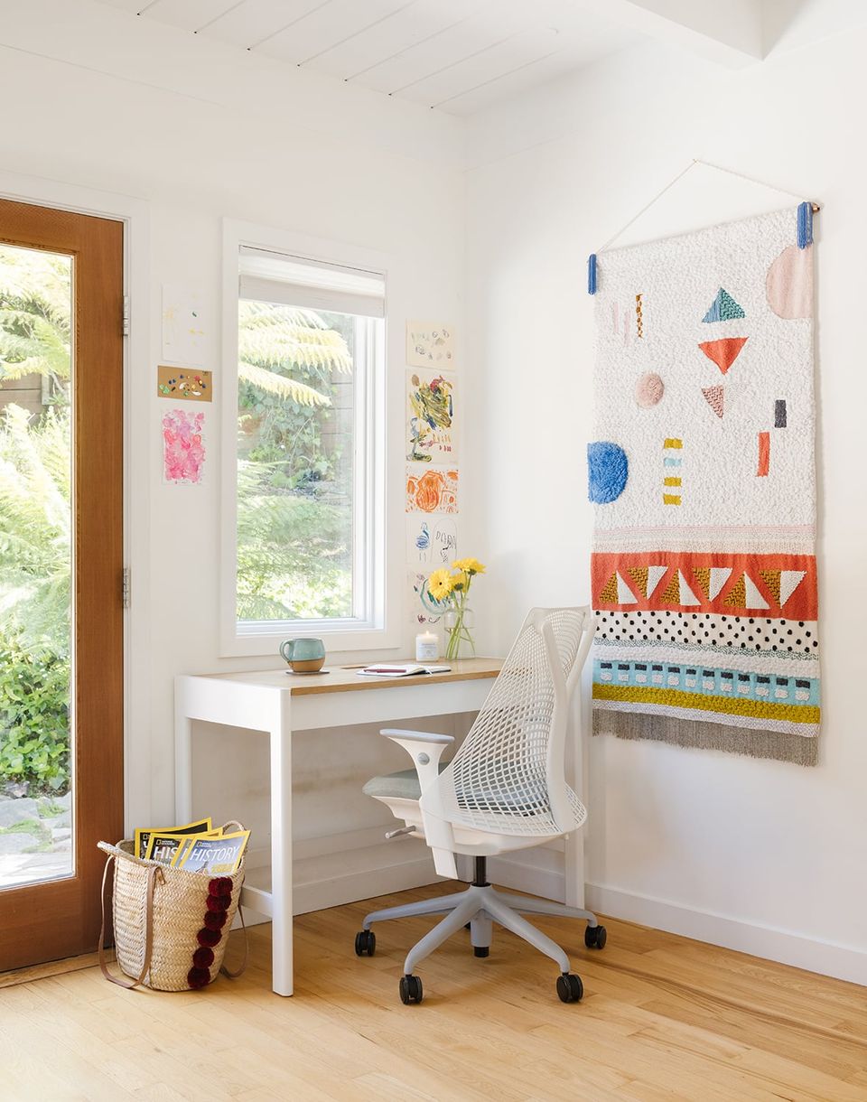 Bright, eclectic home office with colorful abstract wall art, white minimalist desk, and natural wood accents creating a playful, creative workspace