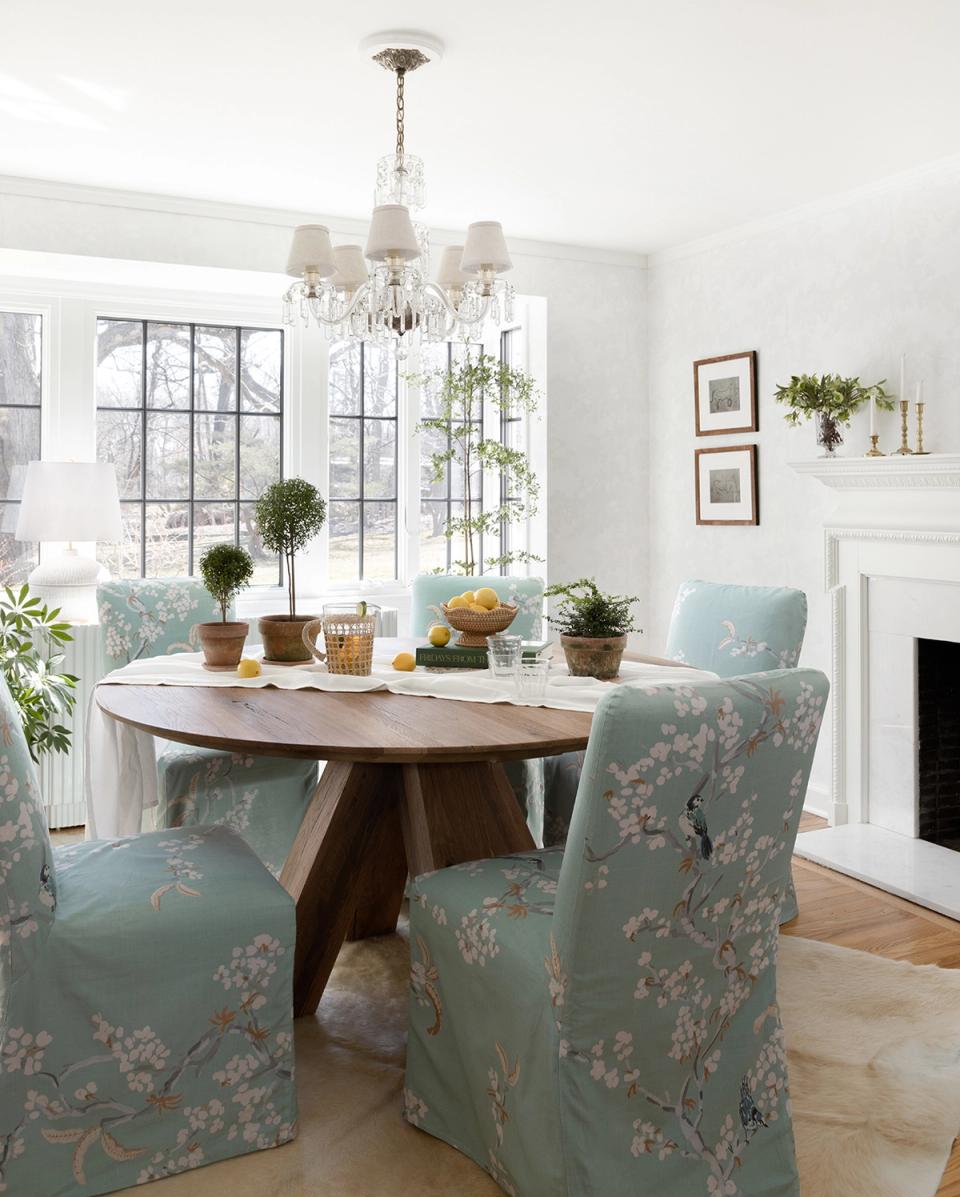Light-filled dining space with round wood table, sage upholstered chairs, and soft botanical touches