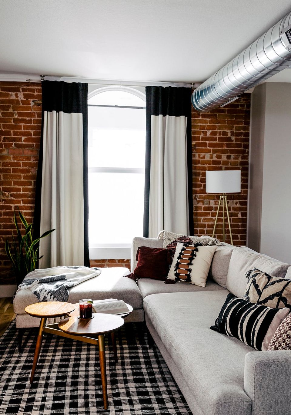 Industrial-chic loft featuring cream sectional, exposed brick walls, black and white geometric patterns, and moody contrast