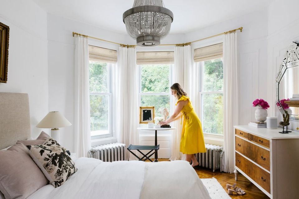 Bright transitional bedroom with bay windows, white bedding, brass accents, and pops of yellow and pink for modern elegance