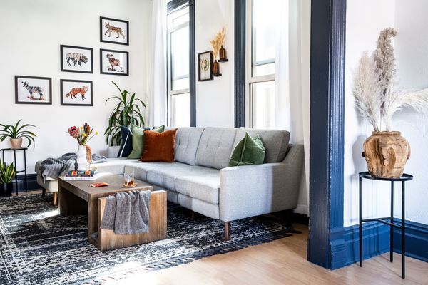 Modern living room with light gray sectional, gallery wall, plants, and geometric patterned rug creating a bright, collected aesthetic