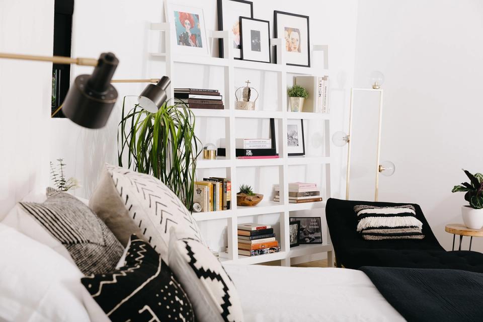 Minimalist bedroom with white shelving wall, monochrome accents, and natural light