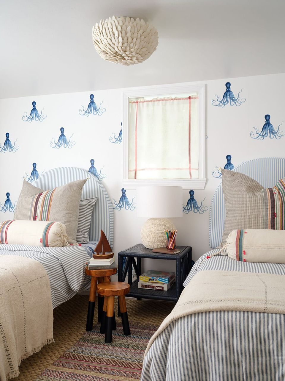 Coastal cottage twin bedroom with blue jellyfish wallpaper, striped bedding, and woven pendant light evoking serene, nautical charm