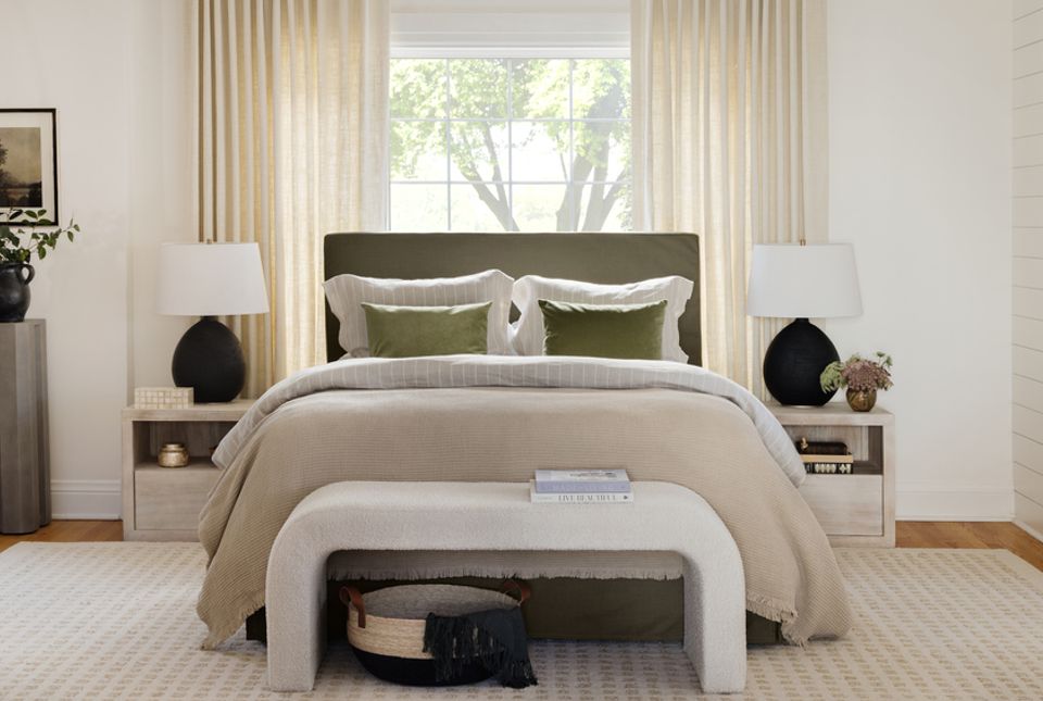 Contemporary bedroom with neutral palette, sage headboard, layered linens, and floor-to-ceiling drapery framing garden views