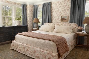 English cottage bedroom with floral wallpaper, gray drapes, and warm traditional furnishings