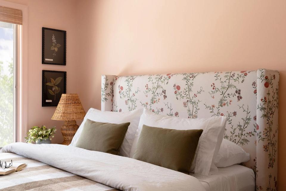 Soft blush pink bedroom with floral upholstered headboard, olive green pillows, and warm natural light creating a romantic, feminine atmosphere.