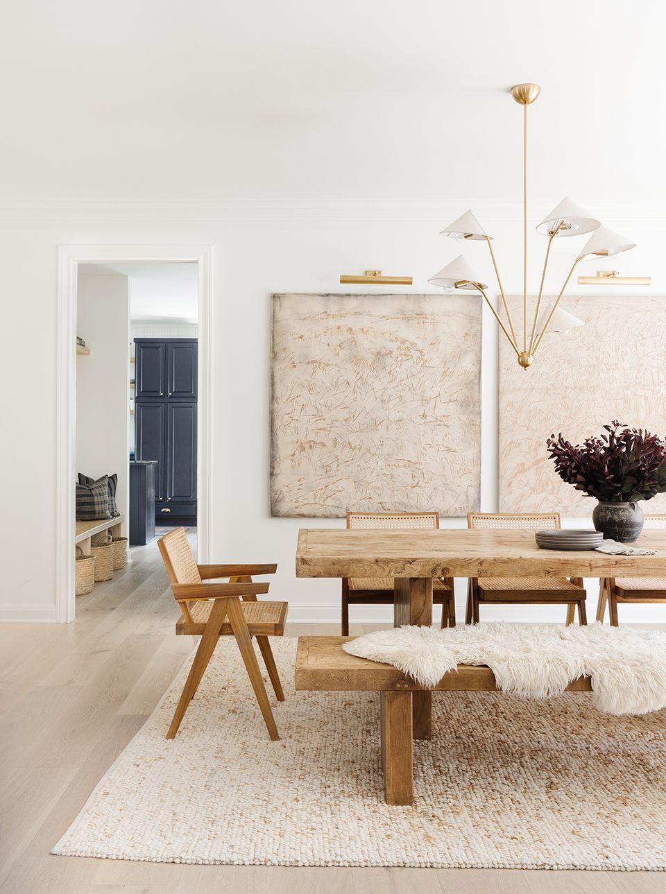 Minimalist Scandinavian dining space with natural wood furniture, neutral textiles, brass chandelier, and serene cream color palette