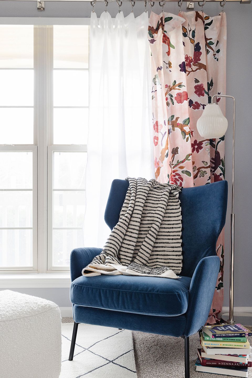 Sunlit window seat with navy wingback chair, striped throw, and romantic floral curtains